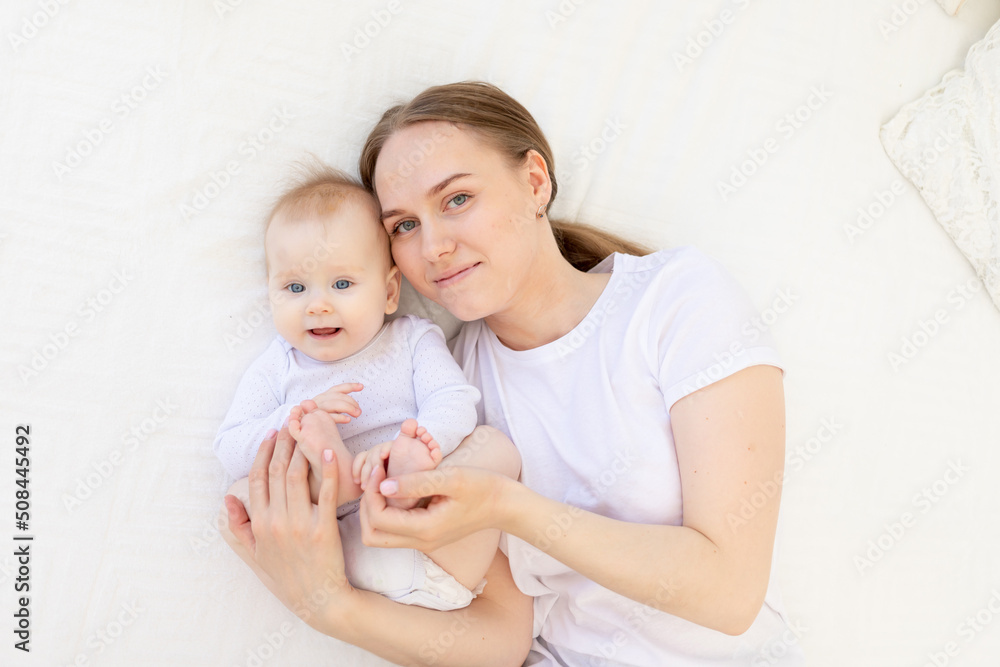 portrait of a mother with a baby in her arms gently embracing him on a white bed at home, mother's love portrait of a mother with a baby in her arms gently embracing him on a white bed at home, mother's love