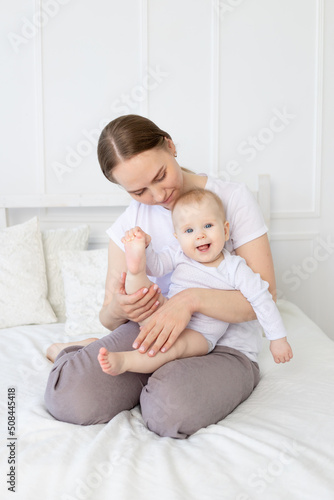 a mother with a baby in her arms gently hugs a smiling child on the bed at home