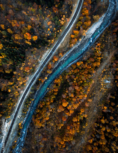 Parallel river and road in autumn forest view from drone