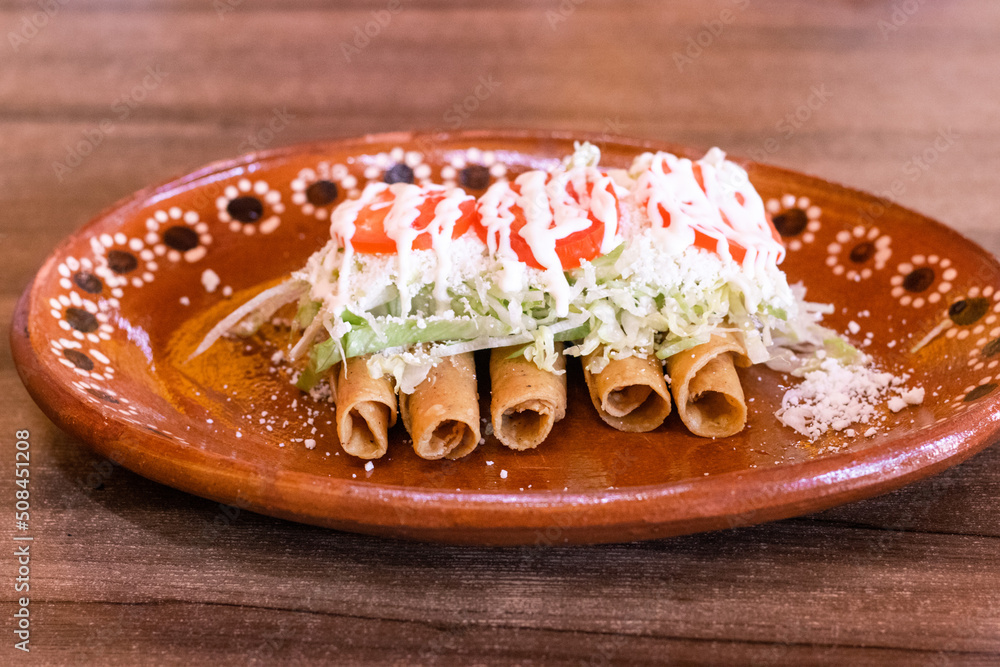 Orden de tacos dorados con lechuga, queso, crema y jitomate Stock Photo