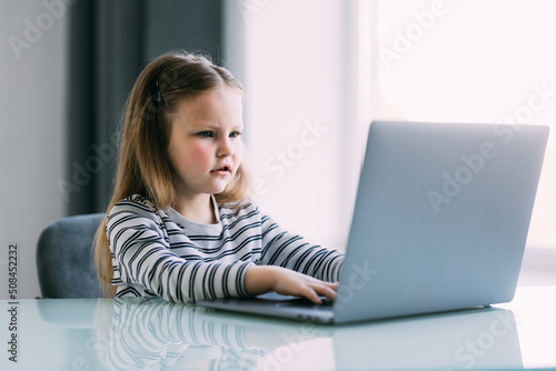 Little girl learning English indoors at online lesson on laptop