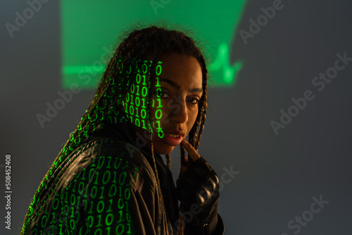 African american woman in leather jacket with projection of computer code on grey background.
