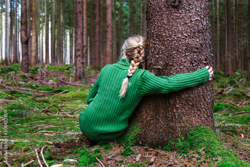 Woman sitting in forest hugging tree, enjoys the silence and beauty of nature.