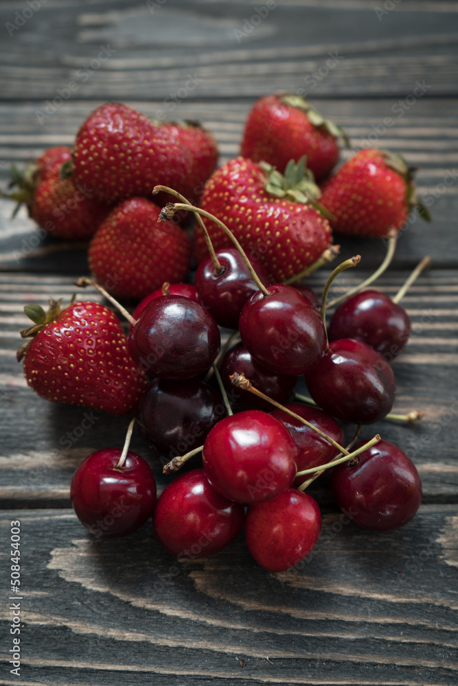 closeup of ripe cherry and red strawberry on wooden background closeup of ripe cherry and red strawberry on wooden background