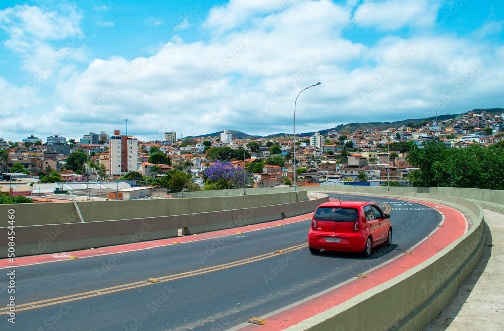 Urban panorama on top of a bridge in the city of Belo Horizonte. Blue sky with clouds. Red car.