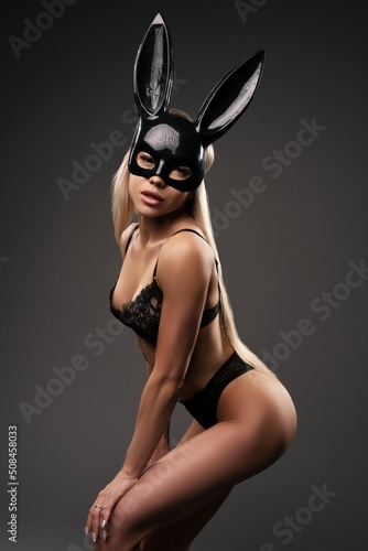 Sexy young woman in underwear and rabbit mask standing in black studio