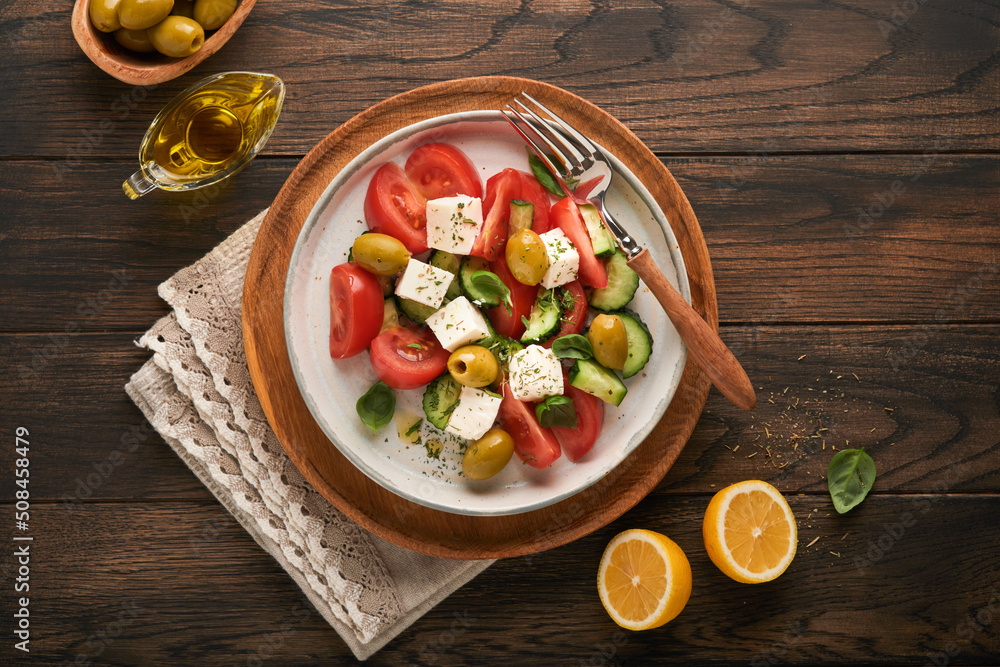 Greek salad. Fresh Greek salad with fresh vegetables, tomato, cucumber, green olives and feta cheese on old dark wooden table background. Top view.