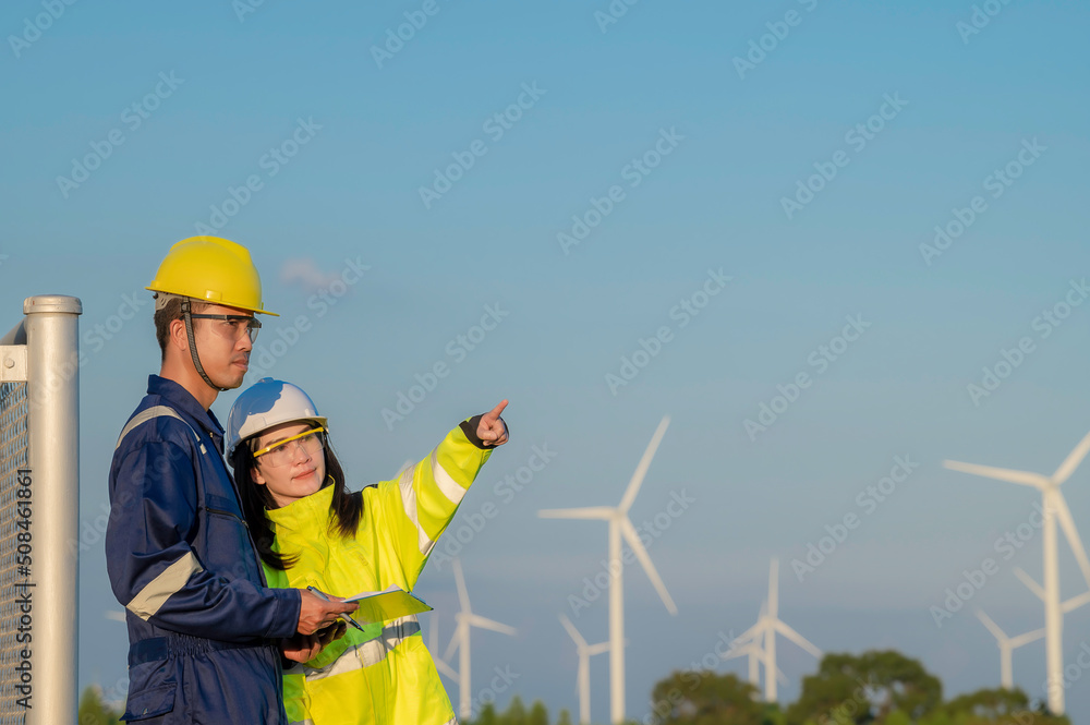 Two engineers working and holding the report at wind turbine farm Power Generator Station on mountain,Thailand people,Technician man and woman discuss about work Two engineers working and holding the report at wind turbine farm Power Generator Station on mountain,Thailand people,Technician man and woman discuss about work