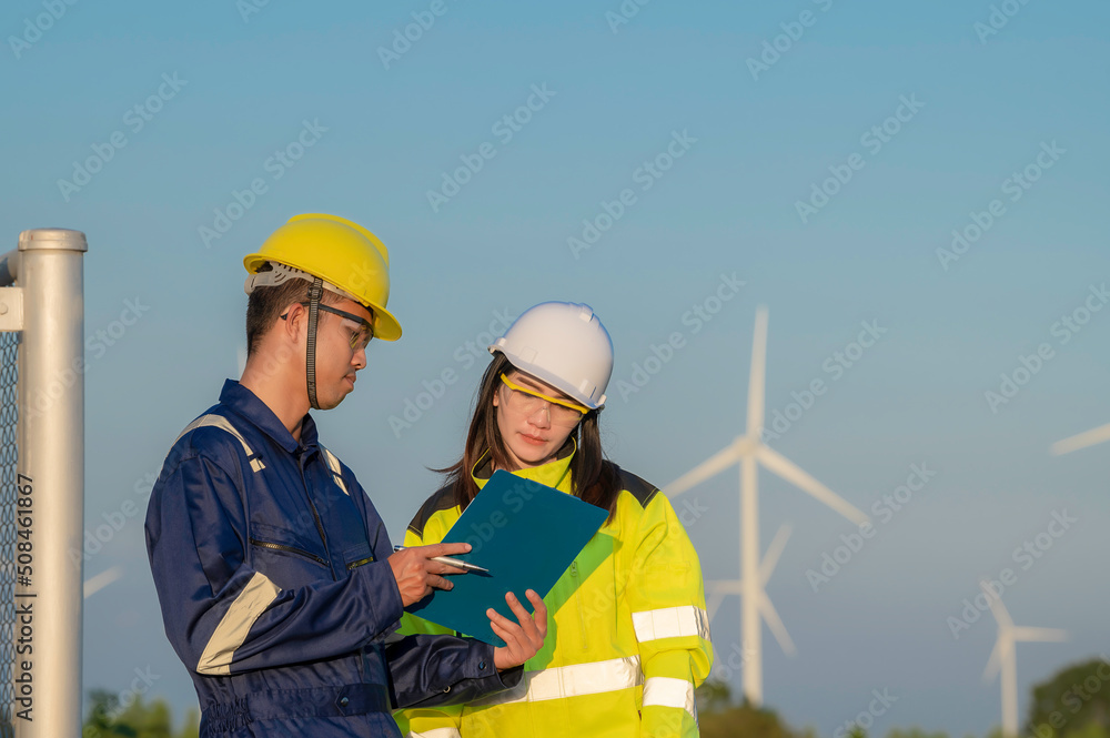 Two engineers working and holding the report at wind turbine farm Power Generator Station on mountain,Thailand people,Technician man and woman discuss about work Two engineers working and holding the report at wind turbine farm Power Generator Station on mountain,Thailand people,Technician man and woman discuss about work
