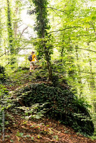 Rear view of young woman in yellow with backpack walking in summer forest among green plants in summer active healthy lifestyle beauty in nature hiking
