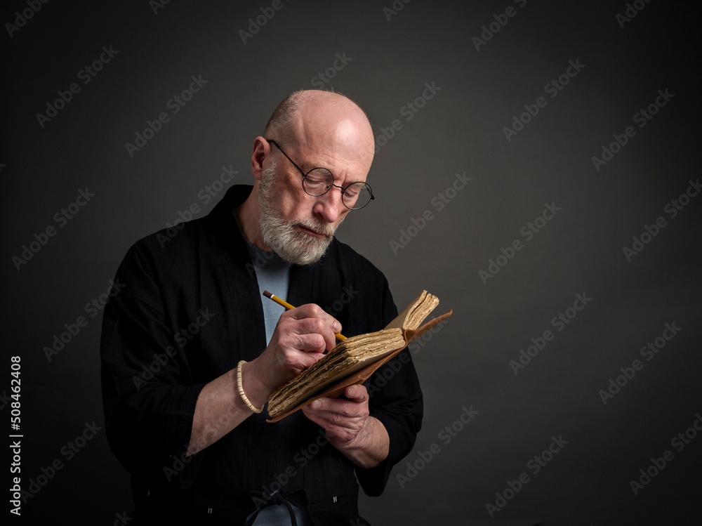 Head and shoulders portrait of bald and bearded senior man in kimono writing a journal Head and shoulders portrait of bald and bearded senior man in kimono writing a journal