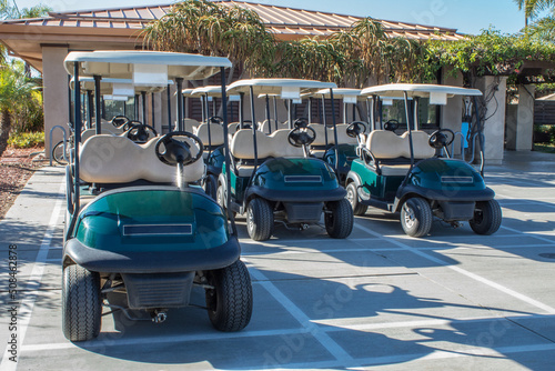 Green golf cars in parking area at a golf course.
