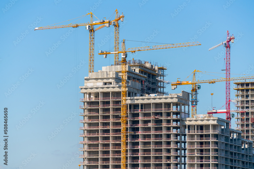 Construction cranes near the facade of a house under construction. modern building industry. Sale and rental of real estate. Construction cranes near the facade of a house under construction. modern building industry. Sale and rental of real estate.