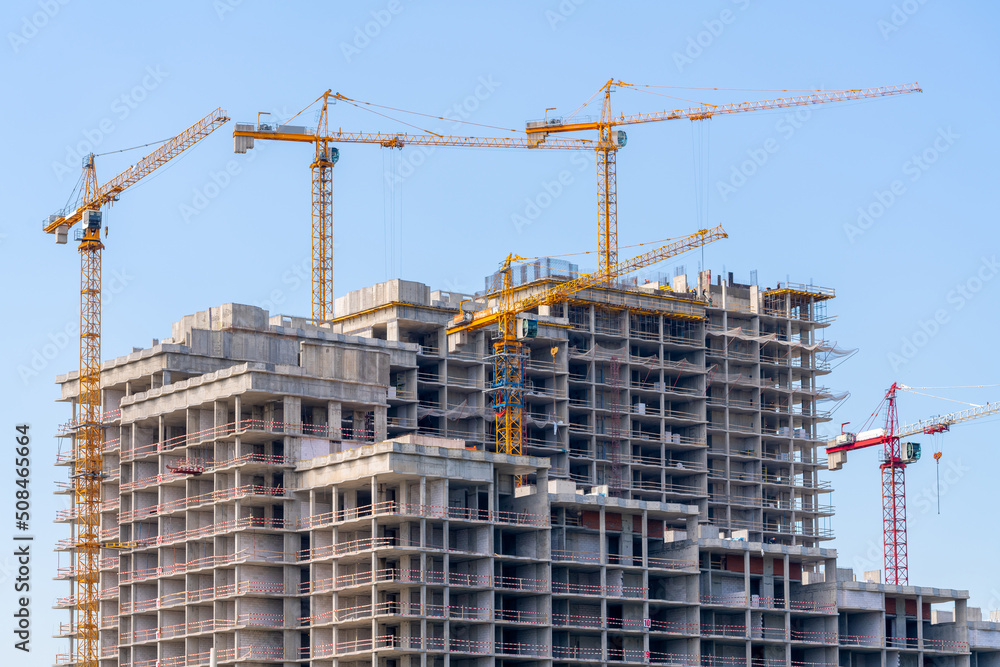 Construction cranes near the facade of a house under construction. modern building industry. Sale and rental of real estate. Construction cranes near the facade of a house under construction. modern building industry. Sale and rental of real estate.