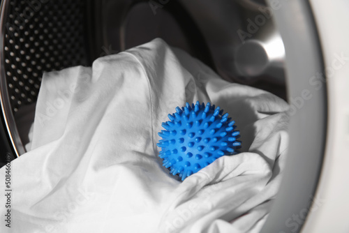 Blue dryer ball and clothes in washing machine drum, closeup