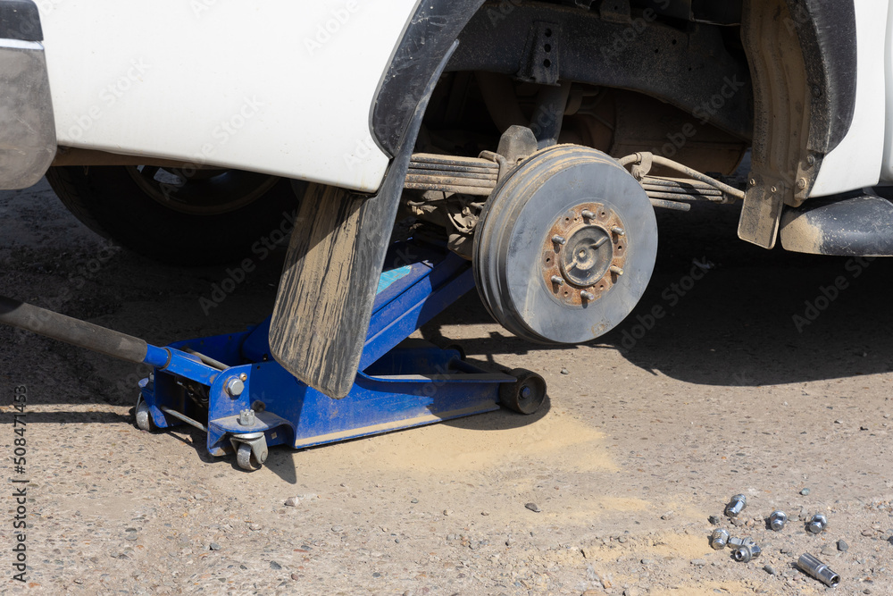 Hydraulic car jack lifted car for tire change. Replacing the wheel on the road tire service center. Car without a wheel lifted on the hydraulic jack in a street Hydraulic car jack lifted car for tire change. Replacing the wheel on the road tire service center. Car without a wheel lifted on the hydraulic jack in a street