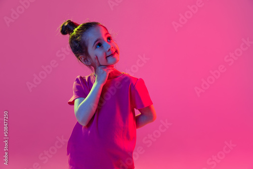 Portrait of cute little girl, kid wearing pink t-shirt posing isolated on magenta color background. Concept of children emotions, fashion, beauty, school and ad concept
