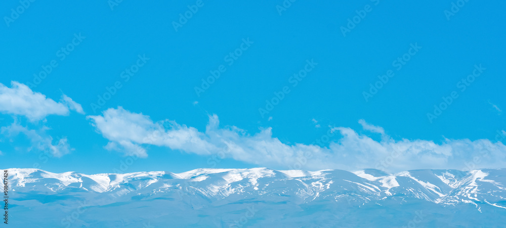 blue mountain sky landscape, snowy peaks of a mountain range in the distance under a clear sky with clouds
