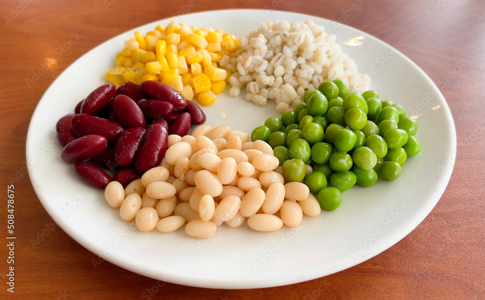top view of navy bean and red bean and corn and  green peas and millet in white plate on wood background
