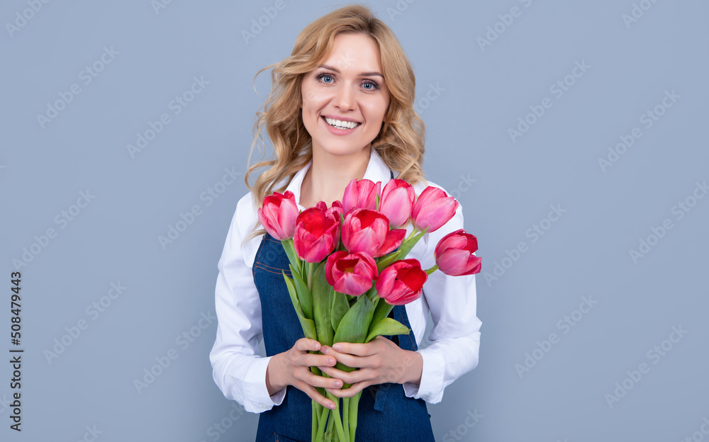cheerful flower seller woman in apron with spring tulip flowers on grey background cheerful flower seller woman in apron with spring tulip flowers on grey background