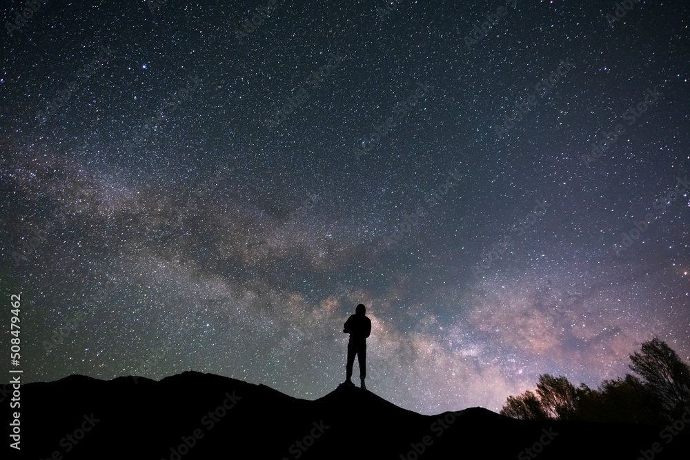 Silhouette traveler on the hill in starry night sky.  Bright milky way galaxy behind him. 