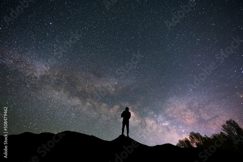 Silhouette traveler on the hill in starry night sky. Bright milky way galaxy behind him. 