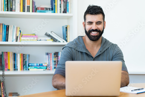 Laughing latin american man with hipster beard at computer