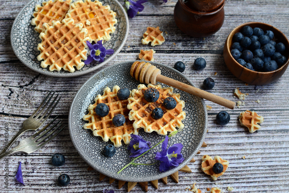 Table with waffles, blueberries, potted honey and lilac bluebells. view from above Table with waffles, blueberries, potted honey and lilac bluebells. view from above