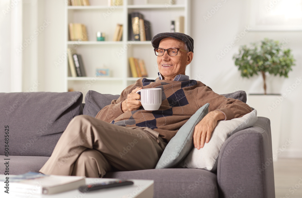 Elderly man relaxing on a sofa at home and holding a cup Elderly man relaxing on a sofa at home and holding a cup