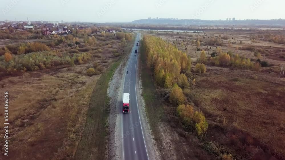 A bird's-eye view of motorcyclist catching up with a lone truck with white cargo trailer driving along the road and overtaking it. International cargo delivery. A bird's-eye view of motorcyclist catching up with a lone truck with white cargo trailer driving along the road and overtaking it. International cargo delivery.