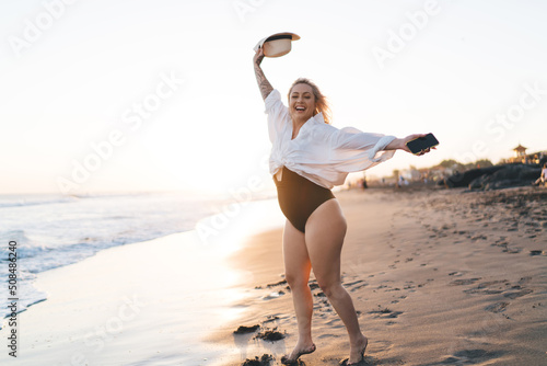 Cheerful plus size woman feeling happiness during summer vacations for visiting seashore and tropical beach, full length of joyful female swimmer with cellphone satisfied duringtravel journey #508486240