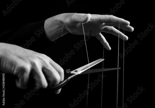 Man cutting strings on hands with scissors. Abuse, violence, slavery cessation. Overcoming addiction and mental health problems. Getting rid of manipulation. Black and white. High quality photo