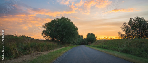 country road among meadows colorful sunset on background