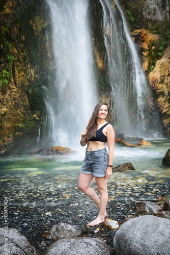 A girl stay under the streams of the waterfall. Grunas Waterfall is a picturesque site inside the National Park of Thethi  Albania