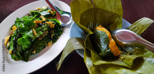 Stir-fried Malindjo Leaves with Egg and  Curry Steamed Seafood in banana leaves with stainless steel poon at south local restaurant. Delicious lunch meal on table. Healthy food   photo