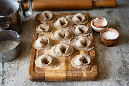 Rye dumplings with meat filling on a wooden board on a gray background. Preparation of dumplings from rye flour dough and pork meat filling. Close-up