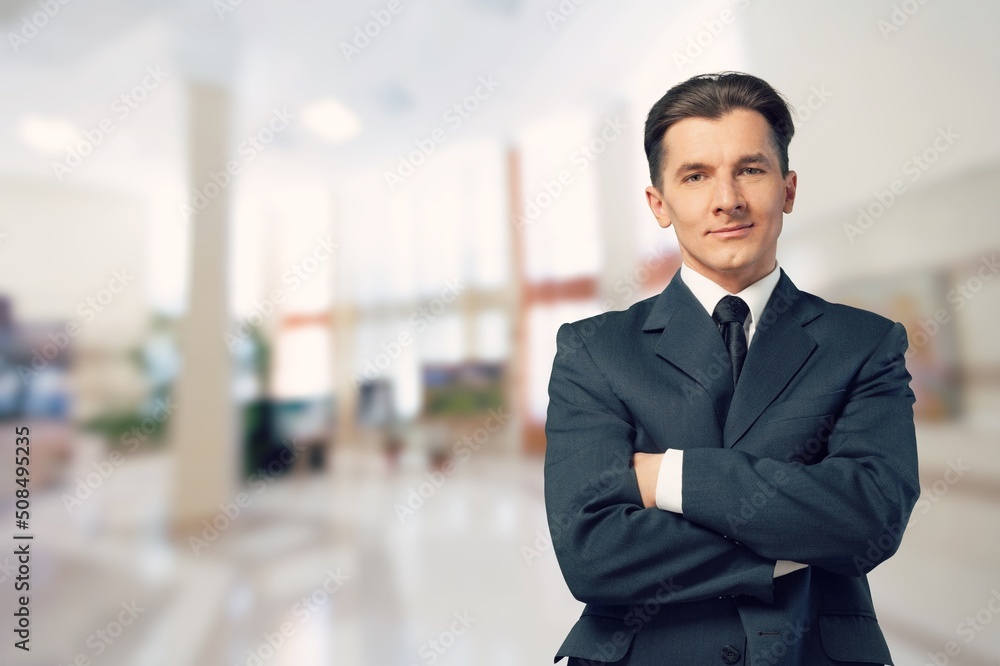 Smiling young businessman in black suit on office background Smiling young businessman in black suit on office background