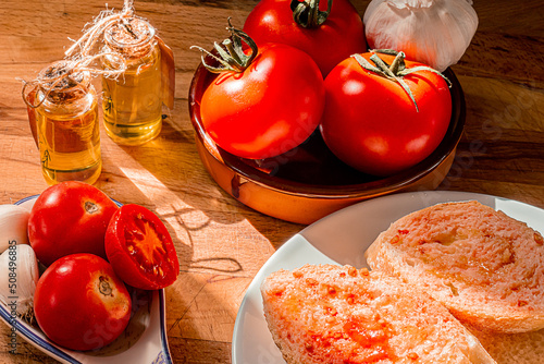 Fototapeta Naklejka Na Ścianę i Meble -  Receta típica Cataluña. Pan con tomate untado y aceite sobre encimera de madera y un bol con ajos. 