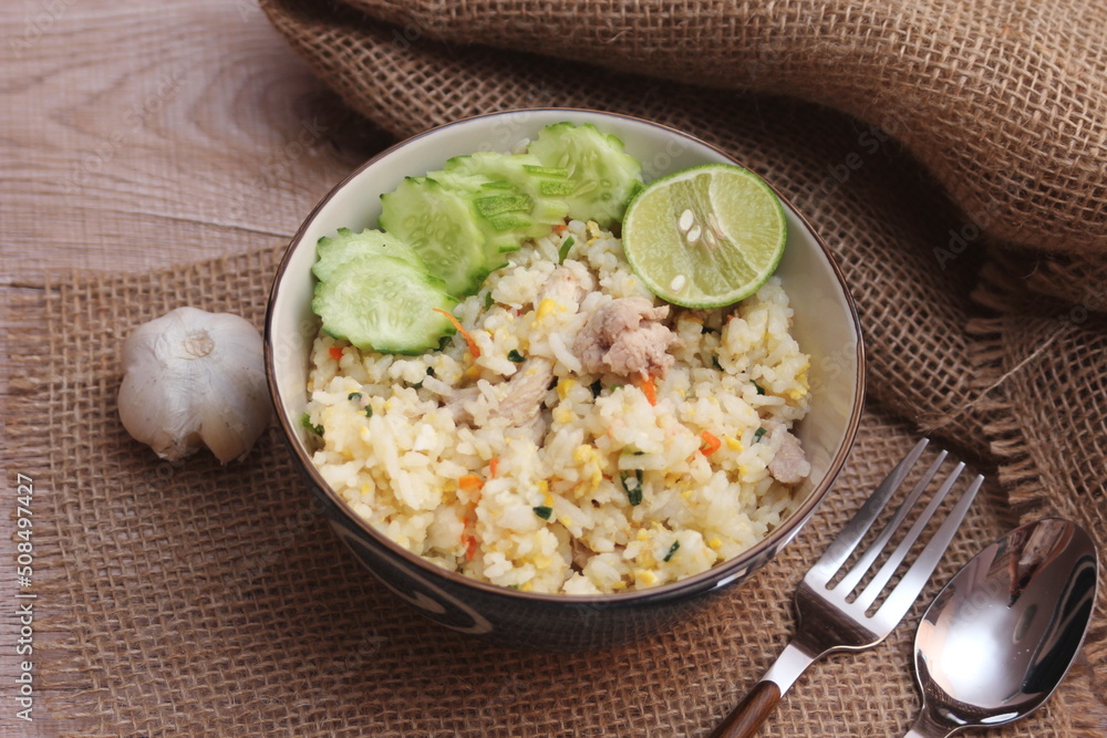 Pork Fried Rice, Chinese Style Fried Rice in a Bowl with Cucumber and Lemon Served on a brown wooden table. Pork Fried Rice, Chinese Style Fried Rice in a Bowl with Cucumber and Lemon Served on a brown wooden table.