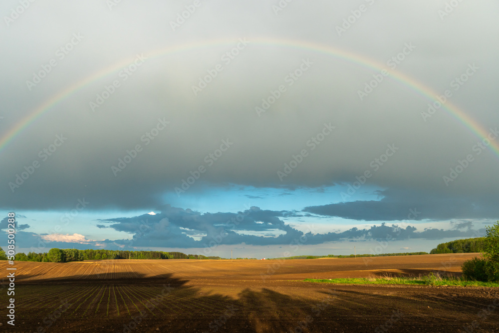 A multicolored rainbow over a plowed agricultural field during the rain. Beautiful spring natural landscape. Beautiful nature of Belarus. A multicolored rainbow over a plowed agricultural field during the rain. Beautiful spring natural landscape. Beautiful nature of Belarus.
