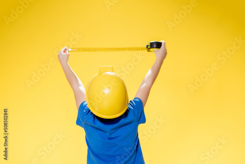 A little boy in a protective construction helmet measures with a tape measure