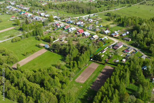 view from the height of the cottage village in summer. Private houses with multicolored roofs have green meadows and trees removed from the drone. Suburban community. Cottage village on the plain