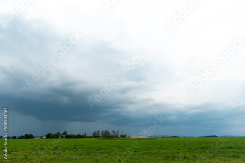 A beautiful thundercloud with rain hovered over a field of wheat. A terrible black cloud on the eve of a tornado and a natural disaster. A hurricane in the countryside. © Pokoman