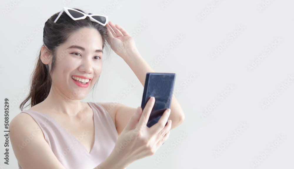 Asian beautiful woman looking on smartphone and raise hand touch on sun glasses and smile with happiness during chatting or shopping online or win a lottery or win game Asian beautiful woman looking on smartphone and raise hand touch on sun glasses and smile with happiness during chatting or shopping online or win a lottery or win game