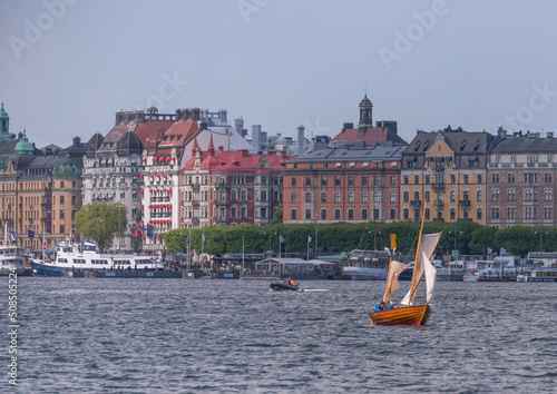 Small open sailing boat with white sail makes a cross in a bay a sunny summer day in Stockholm photo