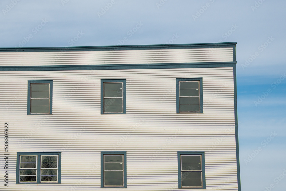 The exterior wall of a vintage white wooden building with bright green trim. The historic country house has multiple single hung glass windows. The wall has a textured horizontal clapboard siding.