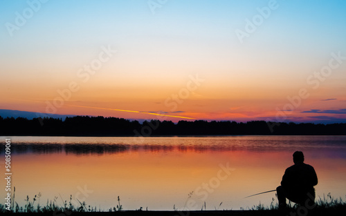 Silhouette of a fisherman with a fishing rod in the morning on a fishing trip. Peaceful sunrise on the lake