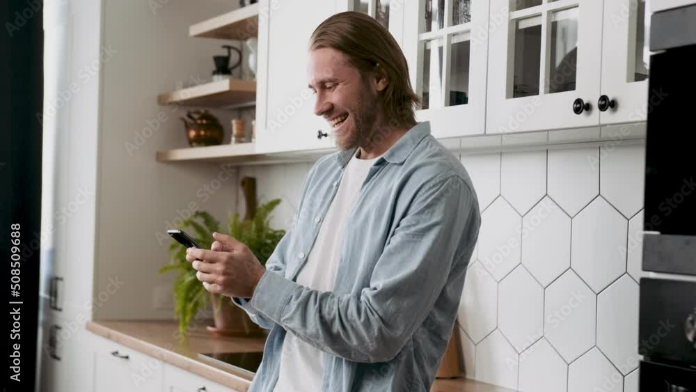 Winner moves a young man exclaiming hooray looking on a smartphone screen with a beautiful smile Winner moves a young man exclaiming hooray looking on a smartphone screen with a beautiful smile
