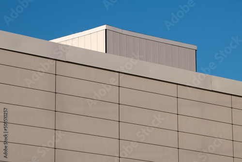 The wall of a commercial building made of precast concrete panels and metal beams. The spaces between the concrete pillars are thin spacing. The cream and textured panels are on a construction site.