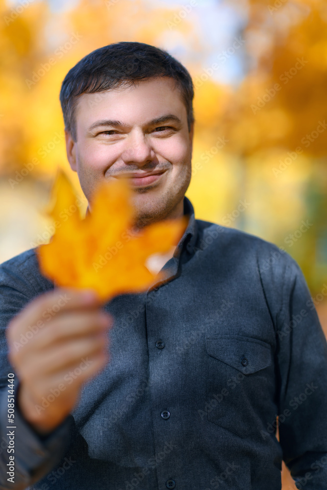 portrait of a man, he looks through a maple leaf, poses in an autumn park, a bright sunny day portrait of a man, he looks through a maple leaf, poses in an autumn park, a bright sunny day
